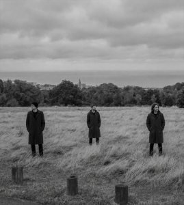 The members of Sojourner standing apart on an open field overlooking Bray Bay beneath a cloudy Irish sky