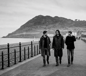 Black and white photograph of Eoin Belfield, Nevan Lochlann and Jesse Rómlárson walking along Bray Seafront with Bray Head in County Wicklow, Ireland in 2017