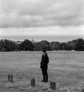Jesse Rómlárson standing alone on a hillside overlooking Bray Bay and the Irish Sea