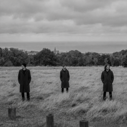The members of Sojourner standing apart on an open field overlooking Bray Bay beneath a cloudy Irish sky