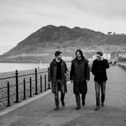 Black and white photograph of Eoin Belfield, Nevan Lochlann and Jesse Rómlárson walking along Bray Seafront with Bray Head in County Wicklow, Ireland in 2017