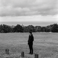 Jesse Rómlárson standing alone on a hillside overlooking Bray Bay and the Irish Sea