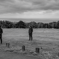 Nevan Lochlann, Eoin Belfield and Jesse Rómlárson standing on a hillside overlooking Bray Bay and the Irish Sea