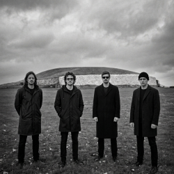 Black and white photograph of Nevan Lochlann, Jesse Rómlárson, Eoin Belfield and J.J. Gilmour standing in front of Newgrange in Ireland in 2017